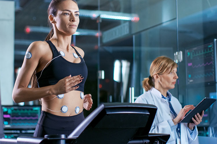 Woman Athlete Runs on a Treadmill with Electrodes Attached to Her Body, Female Physician Uses Tablet Computer and Controls EKG Data Showing on Laboratory Monitors.