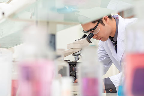 Asian male researcher viewing through a microscope in a laboratory