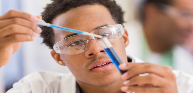 A young African American man holding a test tube with blue liquid
