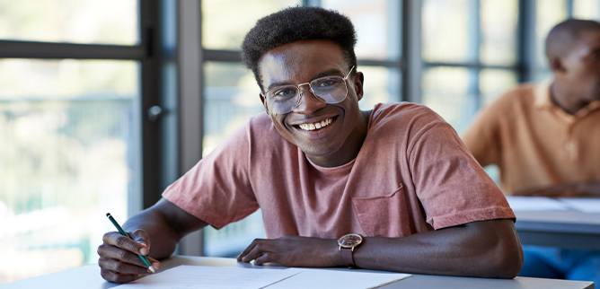 A male student smiling while sitting at a desk