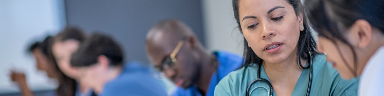 A diverse group of students sit beside each other in the classroom and discuss their course material.