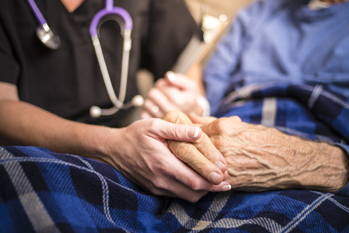 A nurse holding an elderly male patient's hand